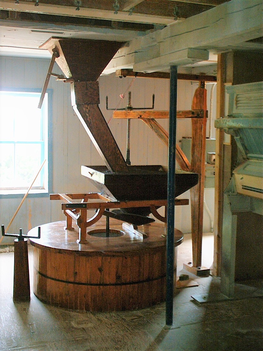 Meules couvertes par la jupe de bois, la trémie et la potence derrière les meules.