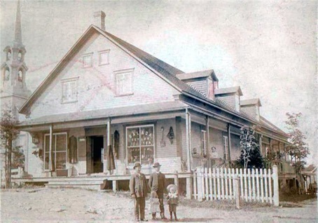 Photo du même bâtiment vers 1906. On y retrouve le magasin général, propriété d’Élie Paradis, d’un style architectural très différent. En juxtaposant les deux photos, on se rend compte que nous sommes en présence du même carré principal auquel un étage et deux tours ont été ajoutés.