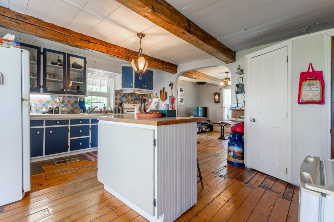 La cuisine telle qu’elle était montrée dans l’annonce de Remax lorsque nous avons acheté la maison en 2021. La prise de vue est la même que sur la photo suivante, les poutres au plafond et l’arche pouvant servir de repères pour constater l’ampleur du changement. Provenance de la photo: Jonathan Roy, photographe.