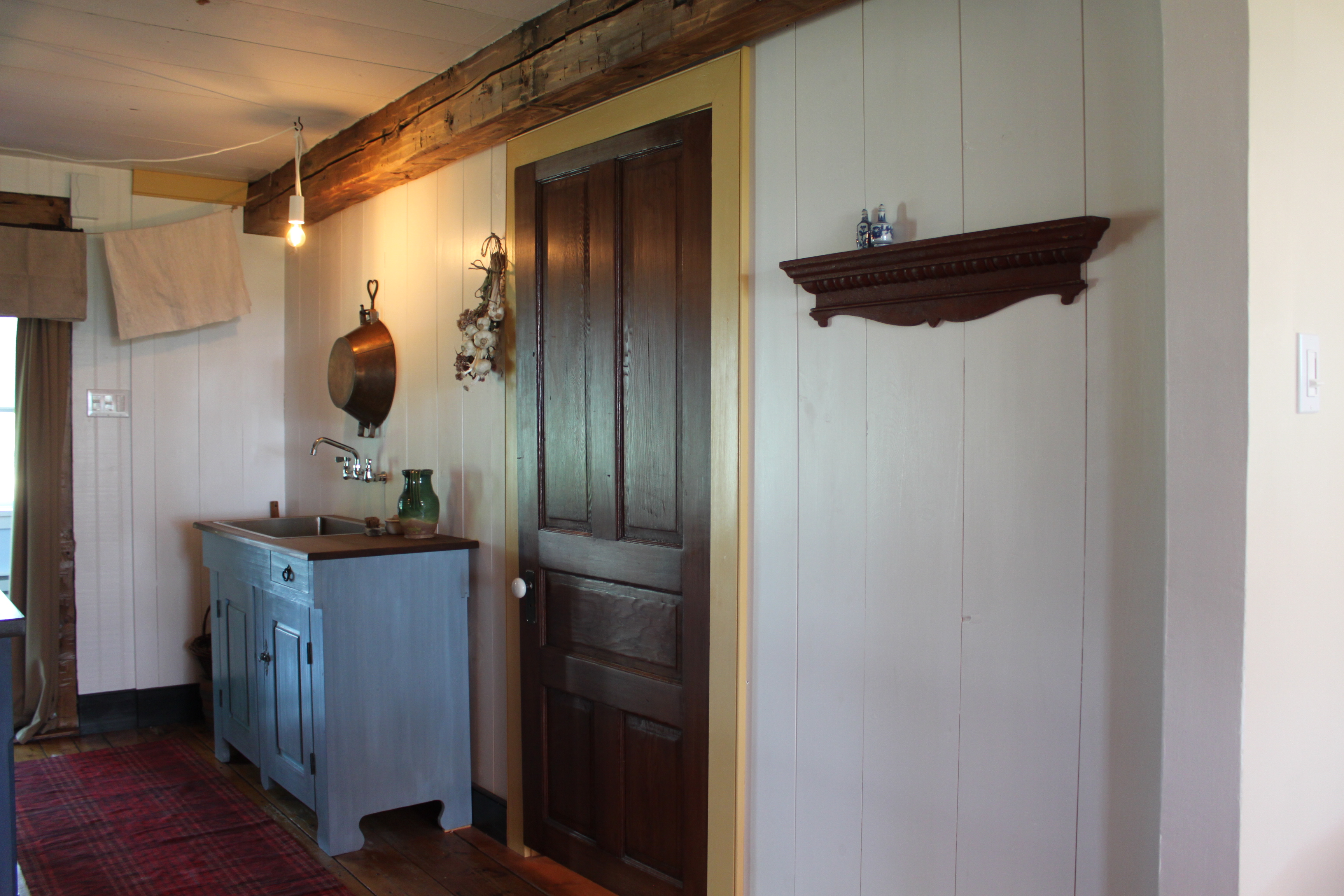 Prise de vue d’une partie de l’espace « cuisine » actuel après transformation au style de l’époque 1790-1820 montrant la reproduction d’évier sec surmontée d’un robinet, la corde à linge de chanvre et la cloison derrière laquelle on retrouve la « pantry » et les modernités.